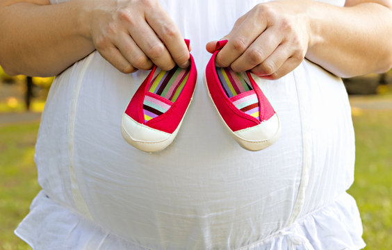 Pregnant mother holding pink baby shoes.