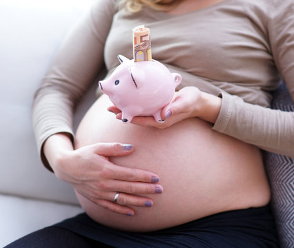 Kinder kosten viel Geld - Schwangere Frau h&auml;lt ein Sparschwein mit einer 5o Euro Banknote &uuml;ber Ihnen Bauch