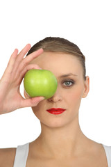 Woman holding green apple over her eye