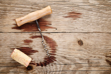 Corkscrew, cork and wine stains on wooden background