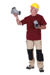 Grey-haired plumber holding two replacement parts