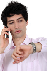 A businessman over the phone looking at his watch.