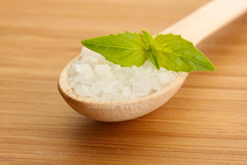 salt in spoon with fresh basil on wooden background