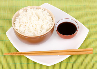 Bowl of rice and chopsticks on plate on bamboo mat