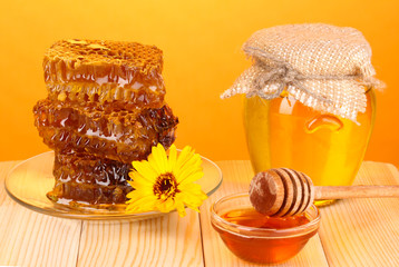 Jar of honey and honeycomb on wooden table on orange background
