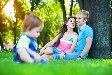 Naklejka na ściany i meble parents with baby in a greenl summer park