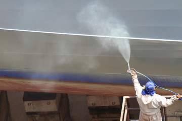 worker painting ship hull using airbrush gray paint