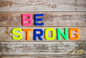 Be strong in colorful plastic letterpress on wood background