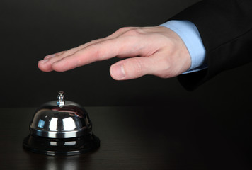 Hand ringing in service bell on wooden table on black