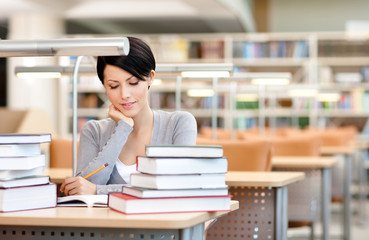 Beautiful student studies with piles of books 