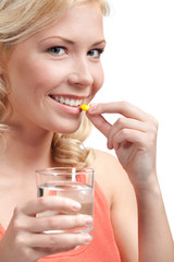 Blond woman with glass of water takes tablets, isolated on white