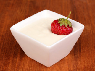 Glass of ripe strawberries with cream on wooden background