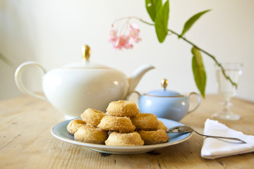a plate of biscuits, a tea pot and a flower on wooden table
