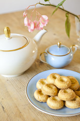 a plate of biscuits, a tea pot and a flower on wooden table