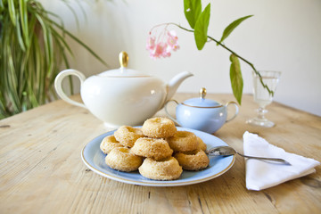 a plate of biscuits, a tea pot and a flower on wooden table