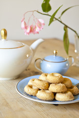 a plate of biscuits, a tea pot and a flower on wooden table