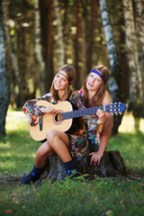 Fototapeta premium Hippie girls with guitar sitting on the stump
