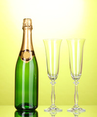 Bottle of champagne and goblets on green background