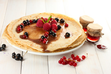 Delicious pancakes with berries and jam on plate on wooden