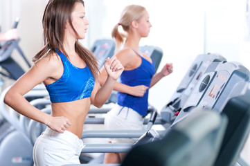 Fototapeta na wymiar Two young women run on machine in the gym
