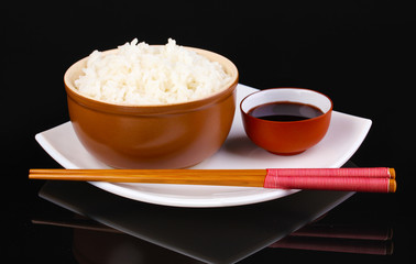 Bowl of rice and chopsticks on plate isolated on black