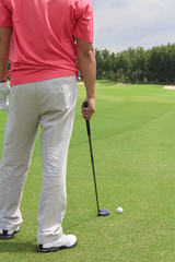 A male golfer standing. Planning for his next shot with a golf c