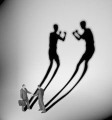 Two businessman casting a shadow shaped like two fighters