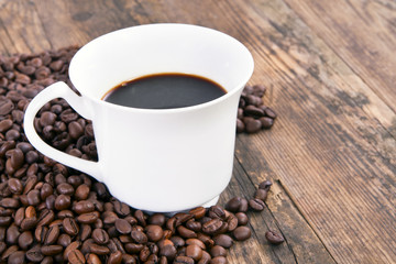 Cup of coffee on wood table with coffee beans around her.