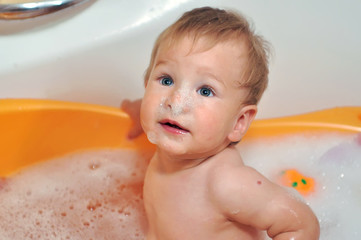 cute one year old boy taking a relaxing bath with foam