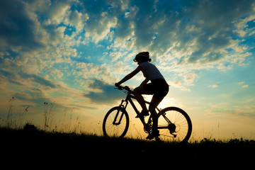 Obraz premium Biker-girl at the sunset on the meadow
