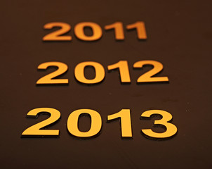 Upcoming years 2011, 2012 and 2013 as golden digits over dark b