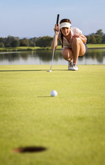 Girl golfer analyzing the green for putting the ball into cup.