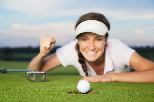 Joyous girl golfer looking at ball dropping into cup.