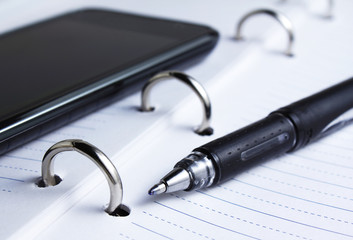 closeup of pen, spiral notebook and cell phone
