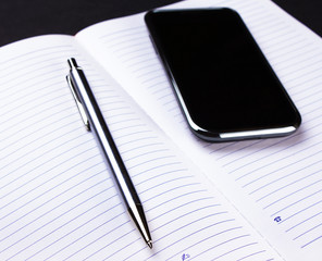 phone, pen and notebook on black