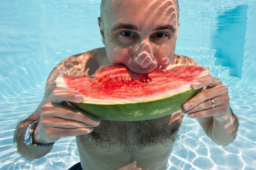 Underwater man eating a slice of watermelon in swimming pool.