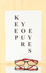 Eyesight test chart with glasses on wooden background close-up