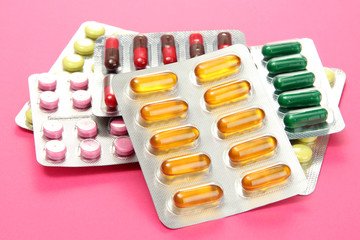 Capsules and pills packed in blisters, on pink background