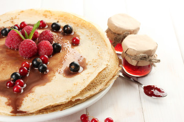 Delicious pancakes with berries and jam on plate on wooden