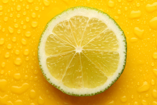 Slice of lime with drop on yellow background