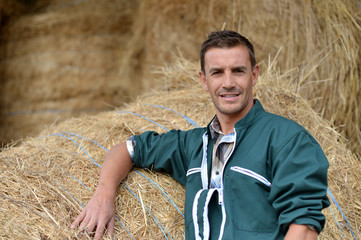 Portrait of smiling farmer standing by haystacks