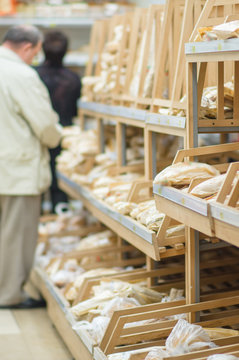 Customers select variety of bread on shelves in supermarket