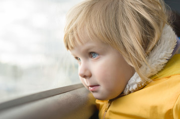 Adorable girl in yellow jacket ride on bus. Look to window