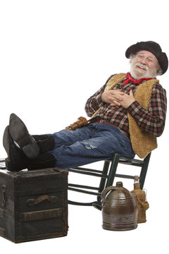 Smiling old cowboy sits in rocking chair with feet up