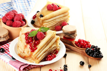 Delicious pancakes with berries, jam and honey on wooden table