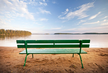 Obraz premium Green bench in front of the lake coast