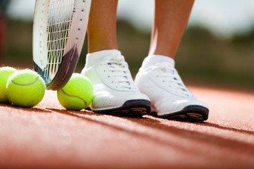 Legs of athlete near the tennis racket and balls