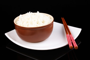 Bowl of rice and chopsticks on plate isolated on black