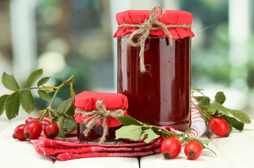 jars with hip roses jam and ripe berries, on wooden table