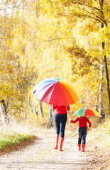 mother with her daughter with umbrellas in autumnal alley